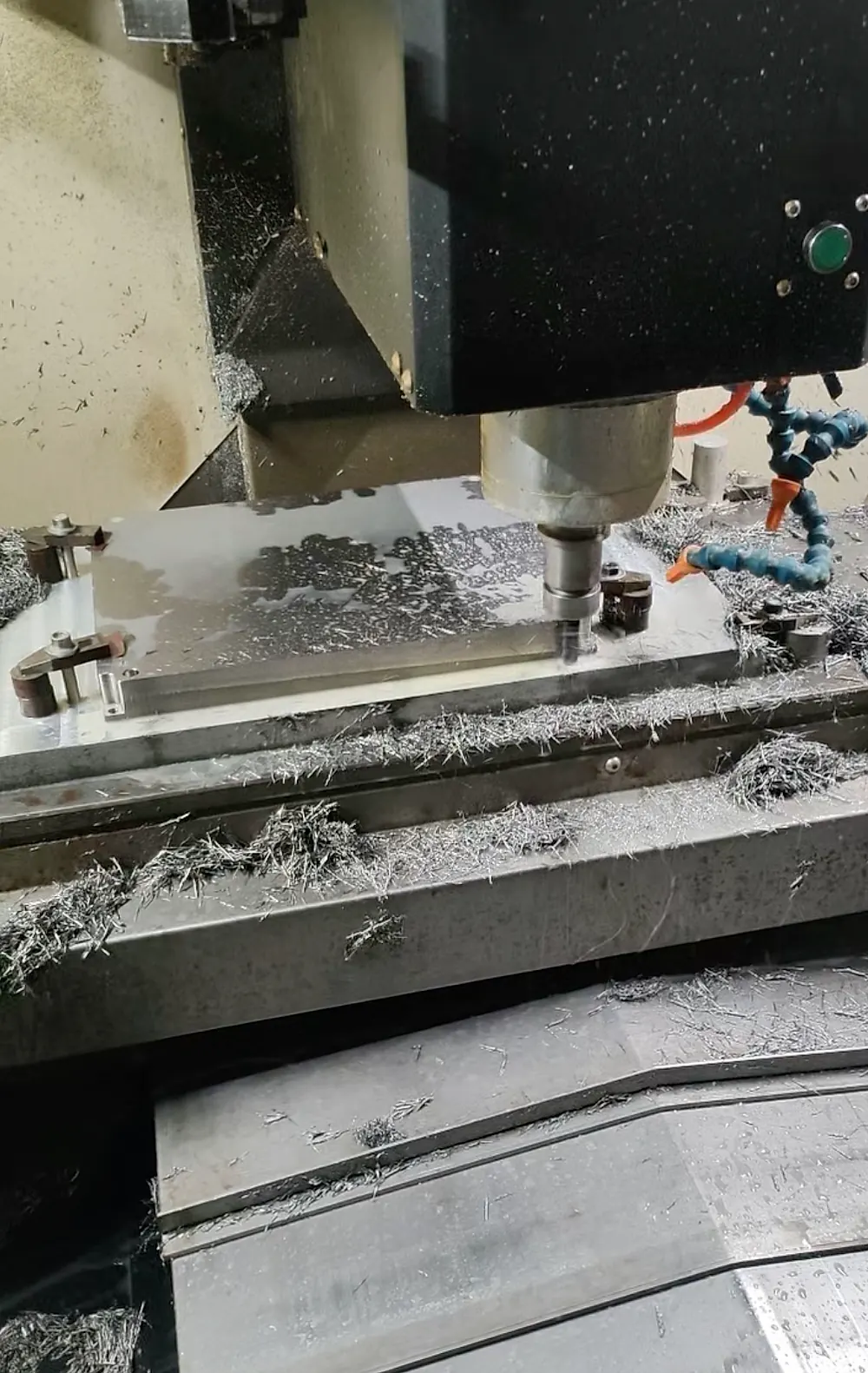 Фрезерный станок с ЧПУ обрабатывает титановую пластину, сопло СОЖ и стружка