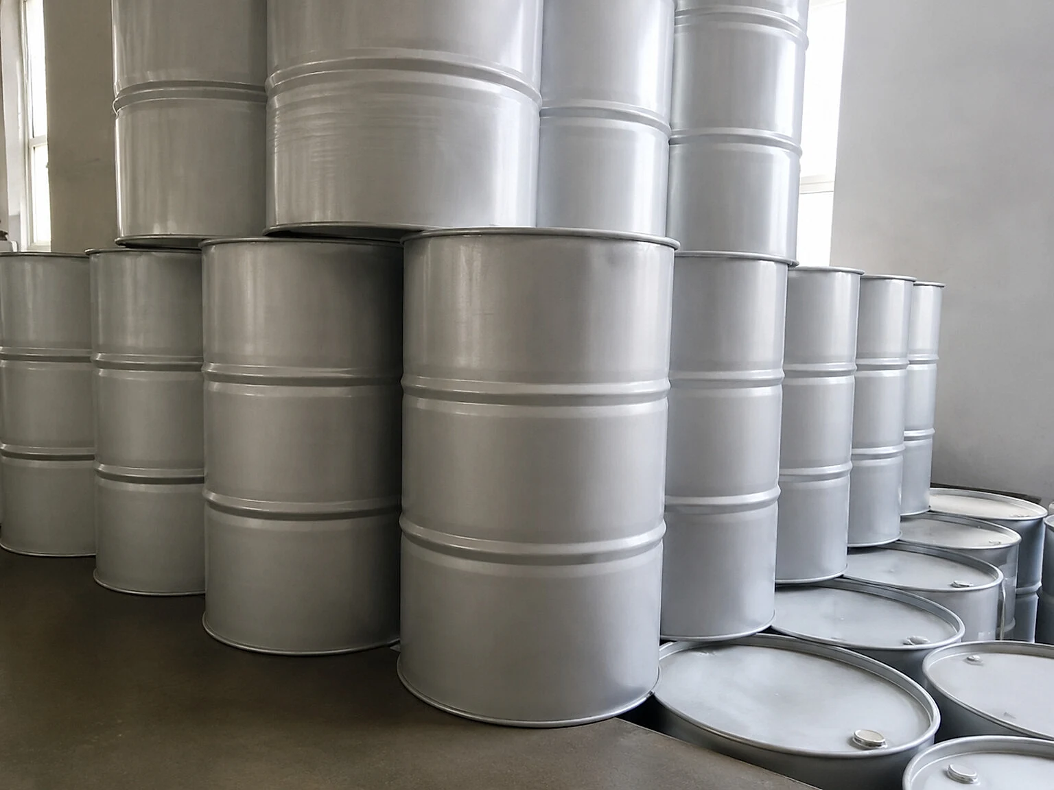 Metal drums stacked in a workshop, representing feedstock, batch identity and storage discipline before a titanium product can be released.